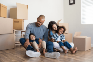 Family of 4 smiling on floor of new home with moving boxes